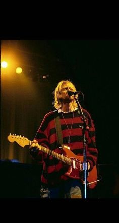 a man standing in front of a microphone while holding a guitar