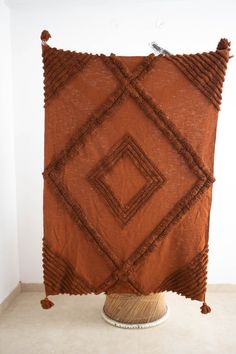 a large brown pillow with tassels on the sides and fringed edges, hanging from a wall