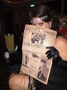 a woman in black dress holding up an old newspaper with pictures on it and wearing latex gloves