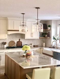 a large kitchen with white cabinets and marble counter tops, along with two pendant lights hanging from the ceiling