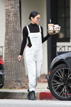 a woman in white overalls and black boots walking past a car