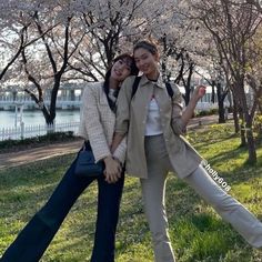 two women standing next to each other in front of trees with cherry blossoms on them