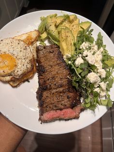 steak, eggs and salad on a white plate with someone holding the plate in their hand