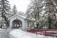 a covered bridge in the middle of winter with snow on the ground and trees around it