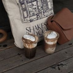 two drinks are sitting next to each other on a wooden table with a bag in the background