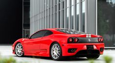 a red ferrari sports car parked in front of a tall building with lots of windows