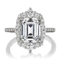 an emerald cut diamond surrounded by white diamonds in a halo setting with two side stones