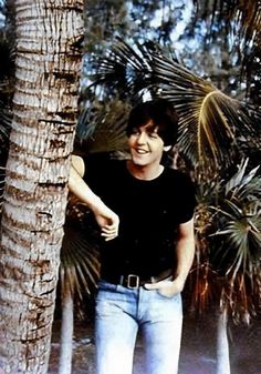 a man standing next to a palm tree in front of some leaves and trees on the ground