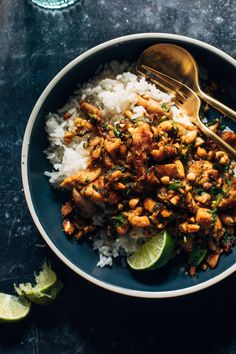 a blue bowl filled with rice and chicken on top of a table next to lime wedges