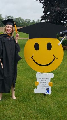 a woman in graduation cap and gown holding up a sign with a smiley face on it