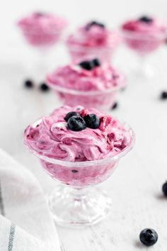 blueberries and yogurt in small glass bowls on a white table with blackberries