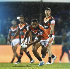 a rugby player is running with the ball in his hand as other players look on