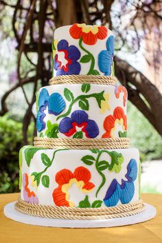 a multi - tiered cake decorated with colorful flowers and jutting rope on a wooden table