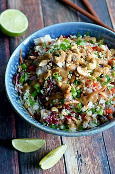 a blue bowl filled with rice, meat and veggies next to lime wedges