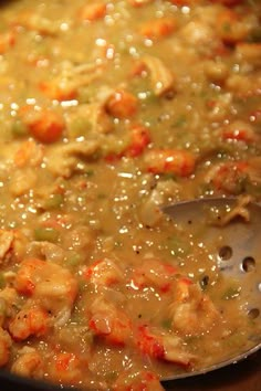 a pot filled with soup sitting on top of a wooden table next to a spoon