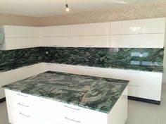 a kitchen with white cabinets and green marble counter tops on the island in front of it