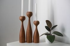 three wooden candlesticks sitting on top of a white shelf next to a potted plant