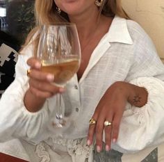 a woman holding a wine glass in her right hand and wearing gold rings on her left wrist