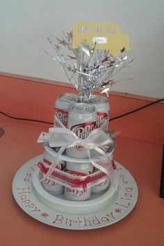 a birthday cake made out of beer cans and wrapped in silver foil with white ribbon