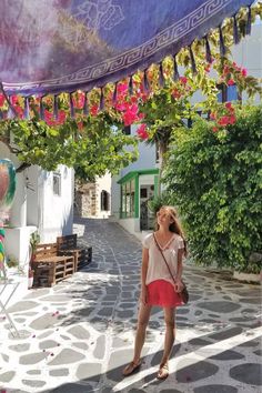 a woman standing in the middle of an alley with flowers hanging from it's ceiling