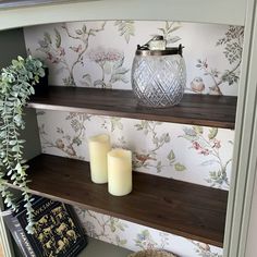 two candles are sitting on top of the bookshelves in front of a wallpapered wall