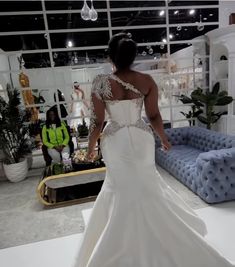 a woman in a white wedding dress is walking through a room with blue couches