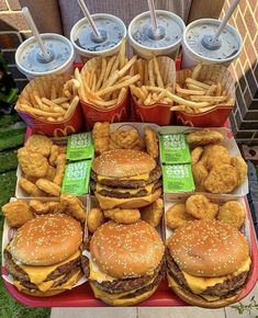 a table topped with lots of hamburgers and fries next to cups of soda on top of each other