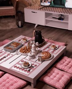 a table with food on it in the middle of a living room, next to a tv