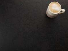 a cup of coffee sitting on top of a black table next to a cell phone