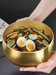 a person holding a gold bowl filled with vegetables and hard boiled eggs in it's center