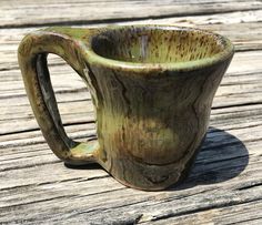 a green mug sitting on top of a wooden table next to a piece of wood