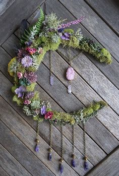 a wreath made out of moss and flowers on top of a wooden floor with beads hanging from it