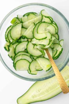 sliced cucumbers in a glass bowl with a wooden pickle on the side