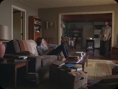 a man and woman standing in the living room next to a couch full of books