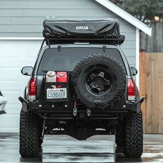 the back end of a black jeep parked in front of a garage