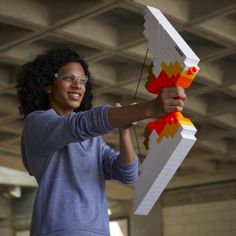 a woman holding up a lego model in the air with an orange and yellow design on it