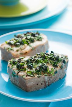 two pieces of meat on a blue plate covered in herbs and seasoning sprinkles