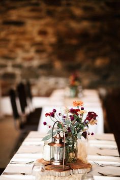 the table is set with white linens and red flowers in vases on it