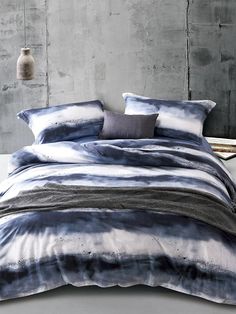 a bed with blue and white comforters in a room next to a lamp on a table