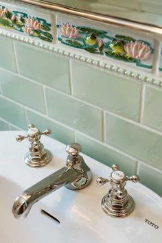 a bathroom sink with two faucets on the side and green tile behind it