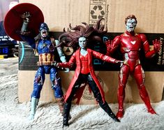 three action figures are posed in front of a cardboard box on a white carpeted surface