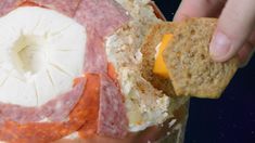 a person holding a piece of bread with cheese and meat on it next to crackers