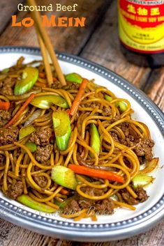 a plate full of beef lo mein noodles with chopsticks on the side and a jar of mustard in the background