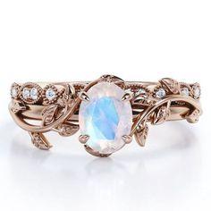 a ring with an oval white stone surrounded by leaves and diamonds on the band, set in 18k rose gold