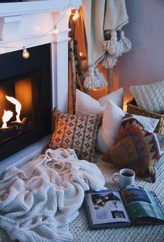 an open book on the floor next to a fire place with pillows and blankets around it