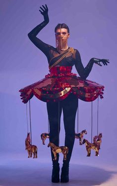 a woman in black and red dress with horses hanging from her legs, holding onto strings