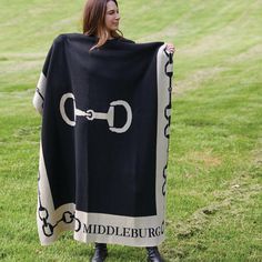 a woman standing in the grass holding a black and white blanket with chains on it