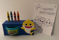 a birthday card with crayons next to it and a toy shark on the table