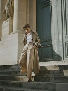 a woman is walking down some steps talking on her cell phone and wearing a trench coat