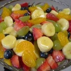 a fruit salad with bananas, oranges, grapes and strawberries in a glass bowl